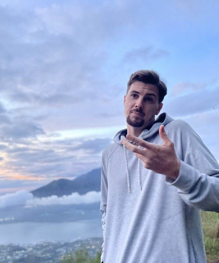 Jarred in a grey hoodie at sunrise above the clouds, mid-gesture